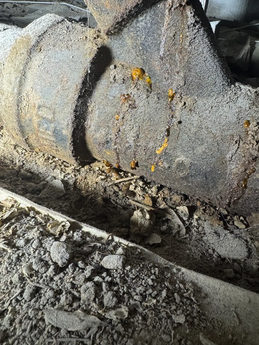 Cracked, rusted cast iron drain pipe under a house