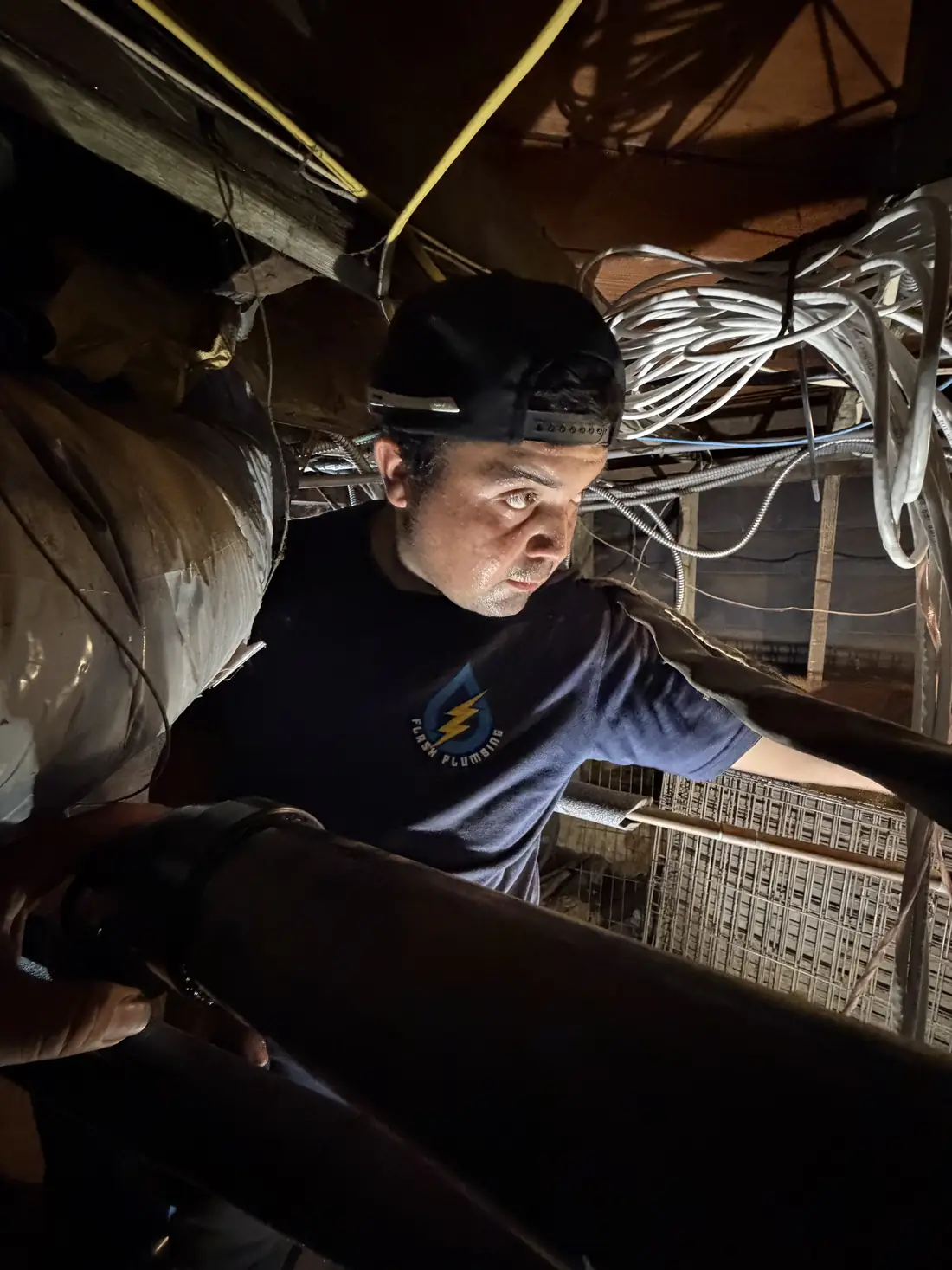 Flash Plumbing technician inspecting pipes in a crawlspace with a headlamp