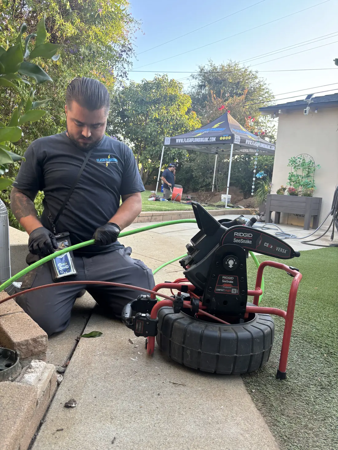 Technician watching a sewer camera monitor while feeding the camera line into a cleanout