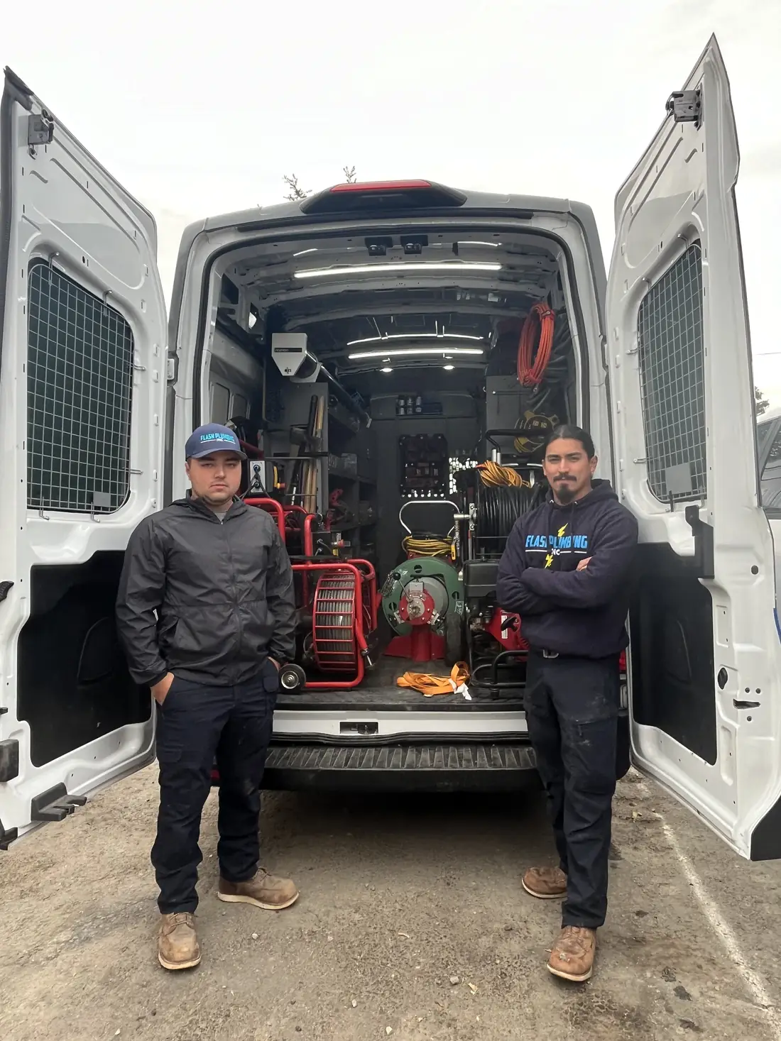 Two Flash Plumbing technicians standing at the open back doors of a fully stocked service van