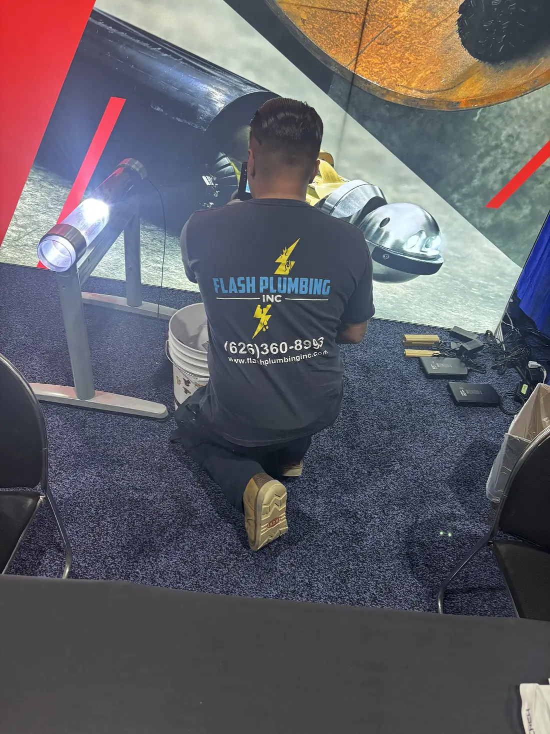 Flash Plumbing technician kneeling with a work light during a job